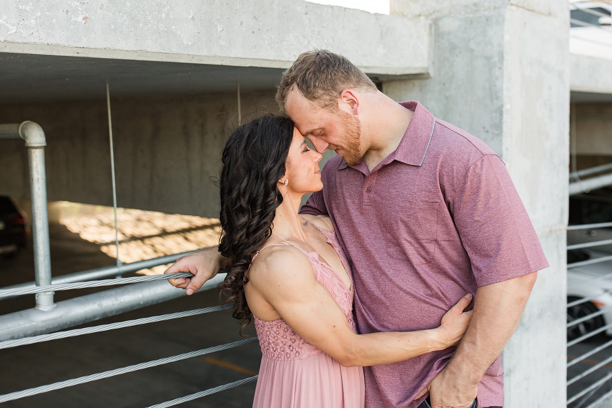 Engaged couple in shades of light pink touch foreheads in a Downtown fargo parking ramp