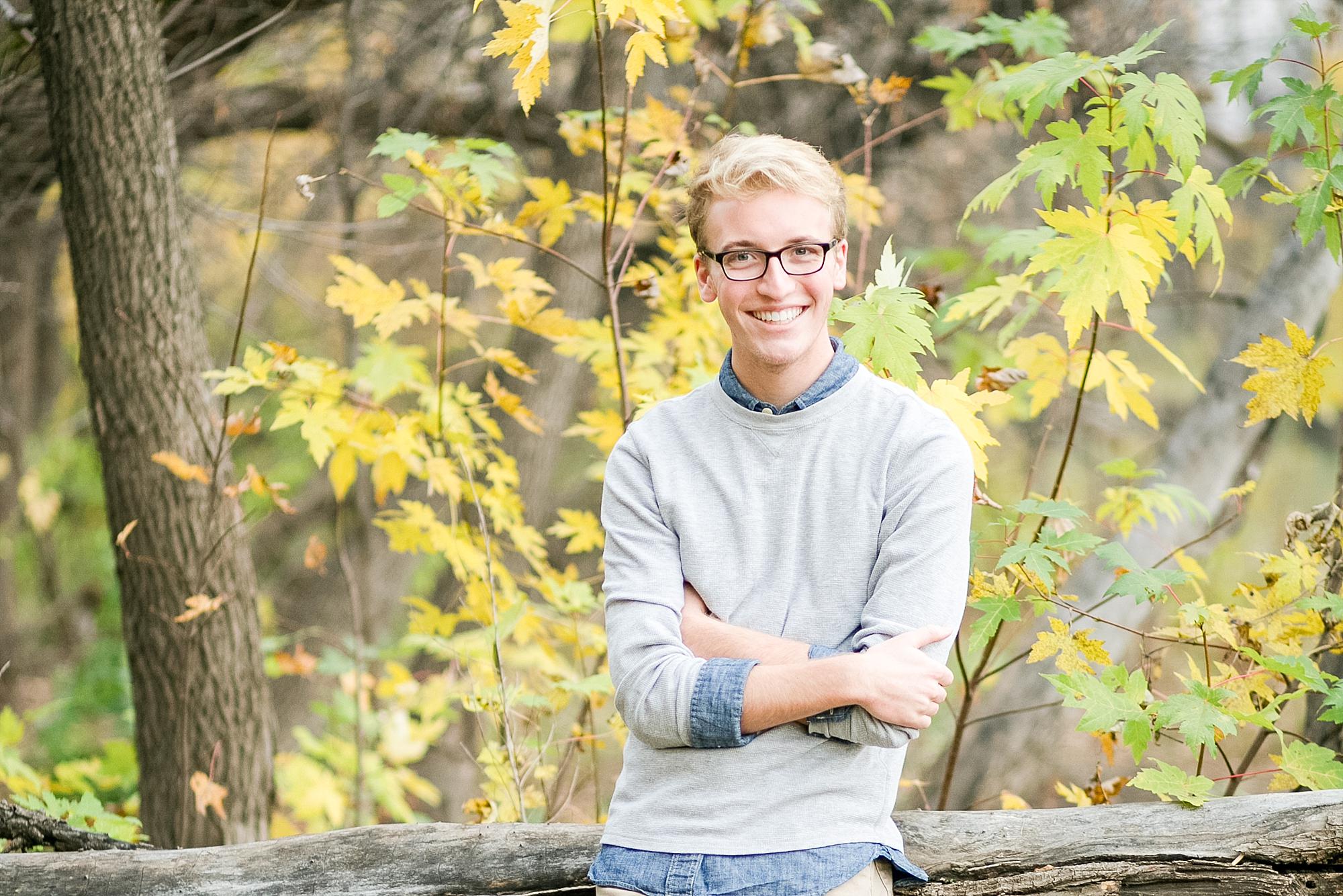 West Fargo Senior smiles and crosses his arms against a tree and the fall leaves