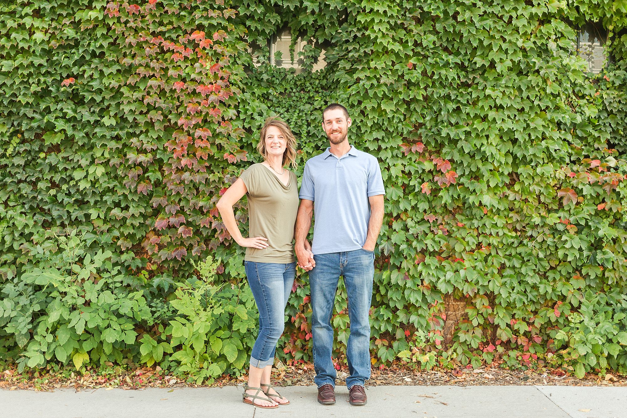 A young couple stand and smile in front of a Downtown Fargo Ivy wall