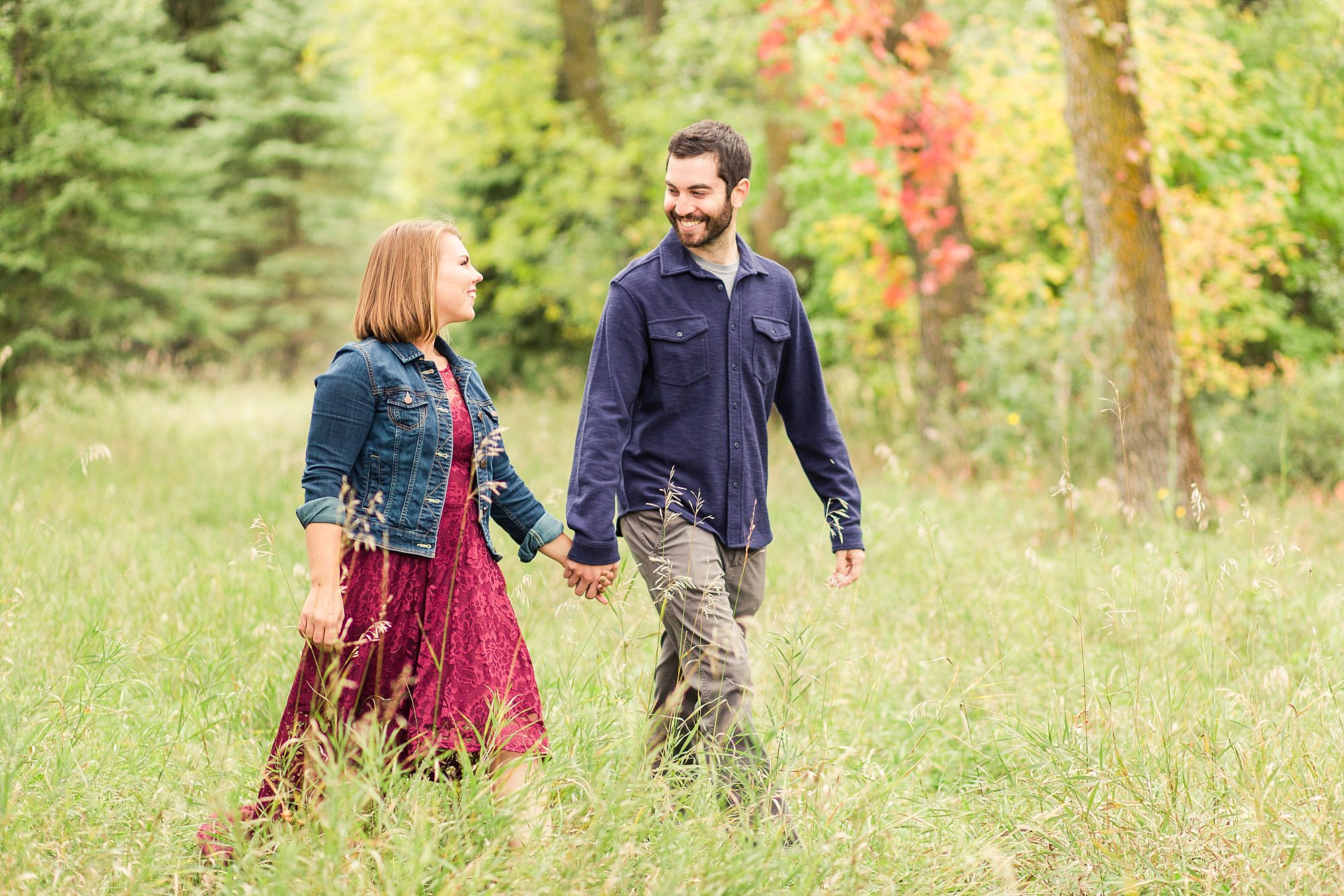Engaged couple hold hands and walk through the tall grass at Riverwood Park