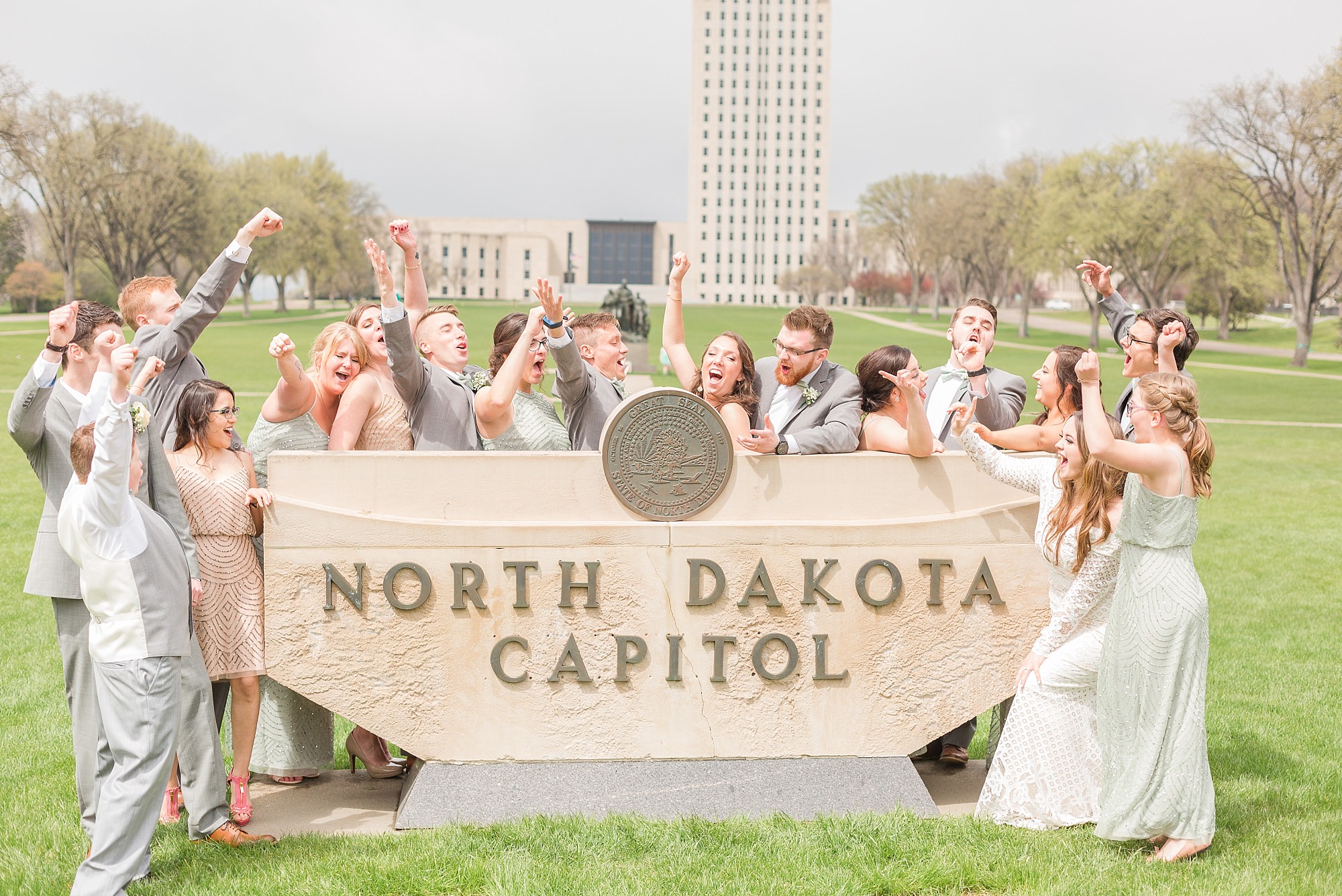 A celebrating bridal party surround the North Dakota Capitol sign