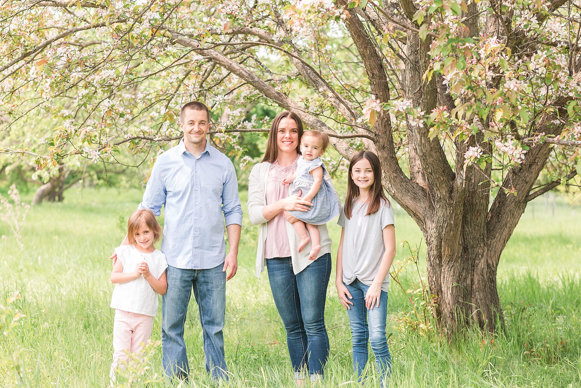 A couple smile with their three daughters for spring photos in orchard glen