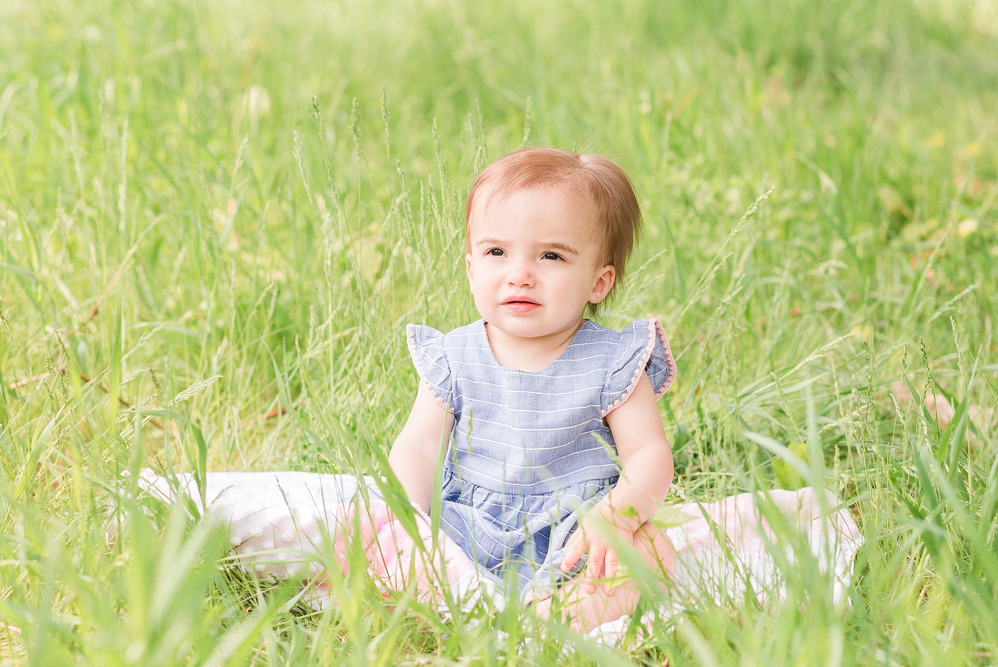 A one year old girl looks at the camera in a blue and pink dress
