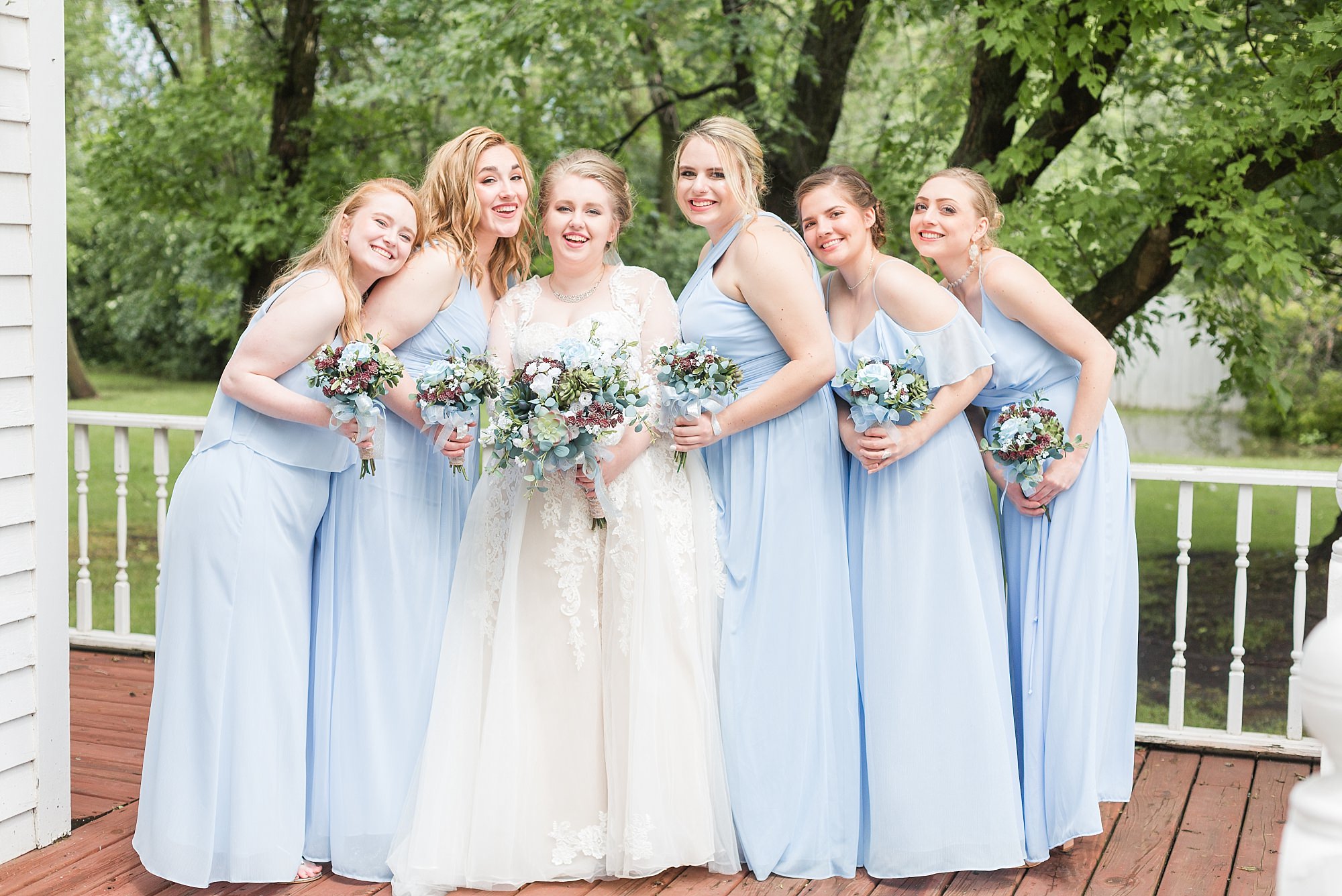 Bridesmaids in light blue surround a bride in a lace dress