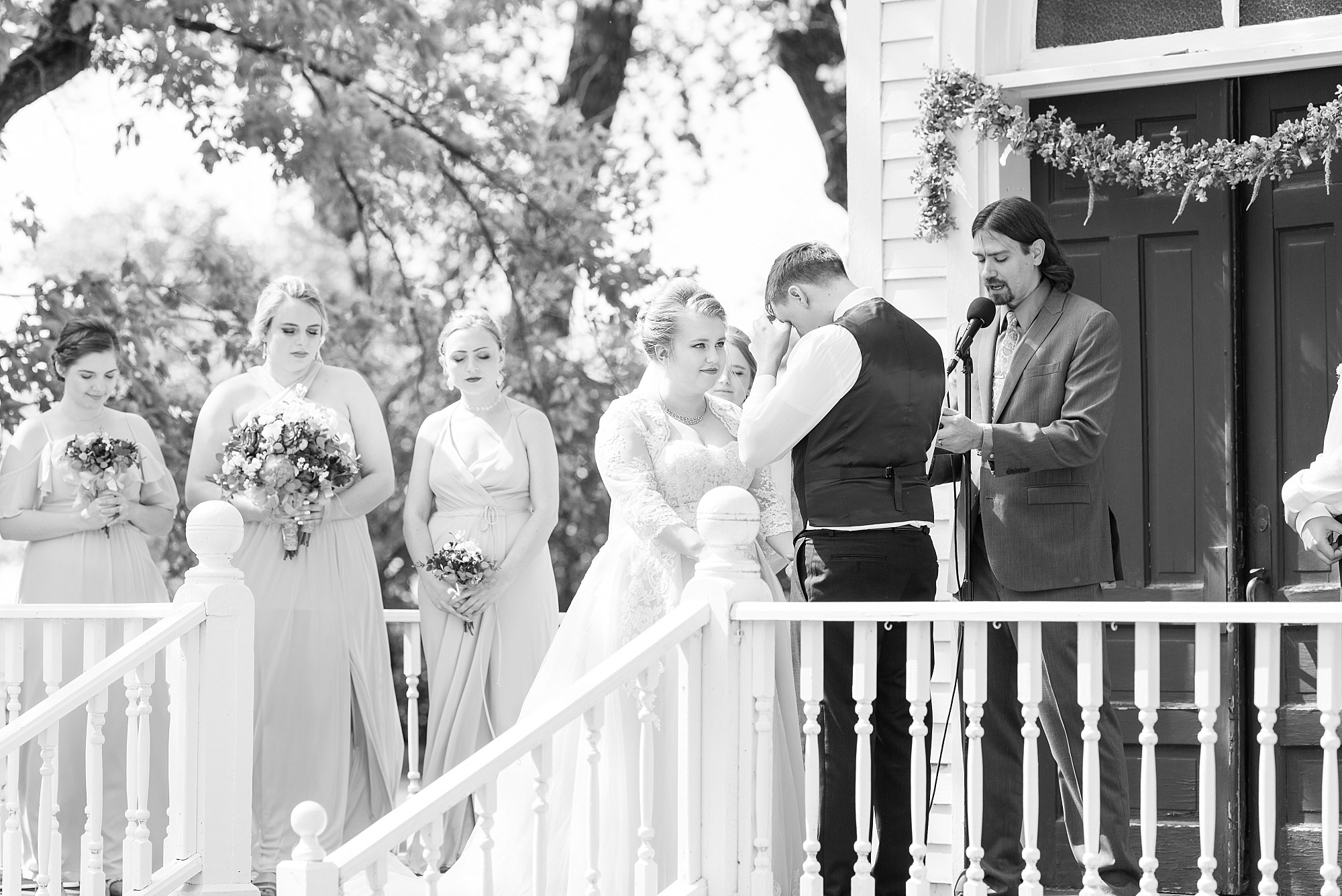 A groom wipes away a tear during an outdoor ceremony in front of a small church