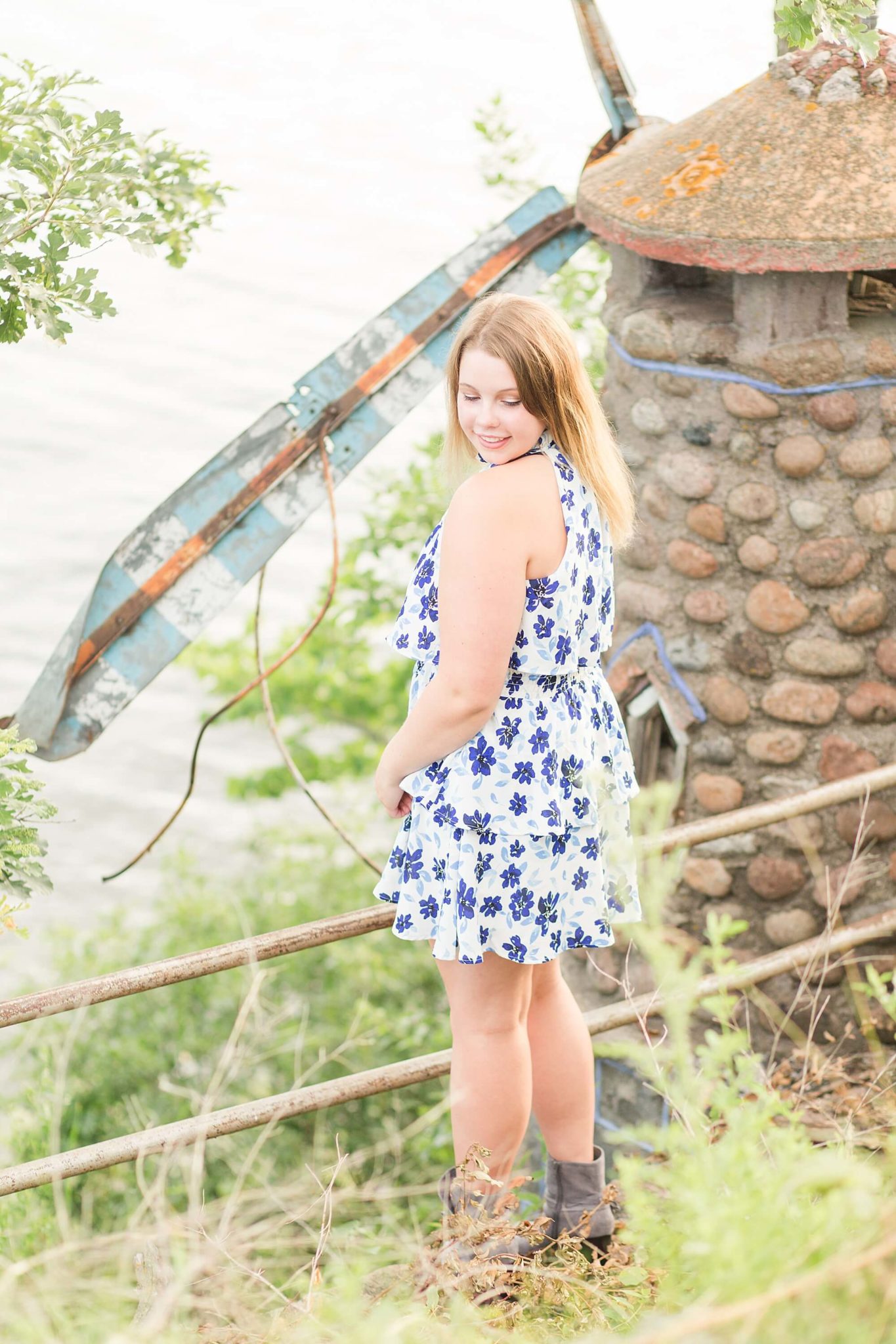 A high school senior smiles down at her floral dress along the lake