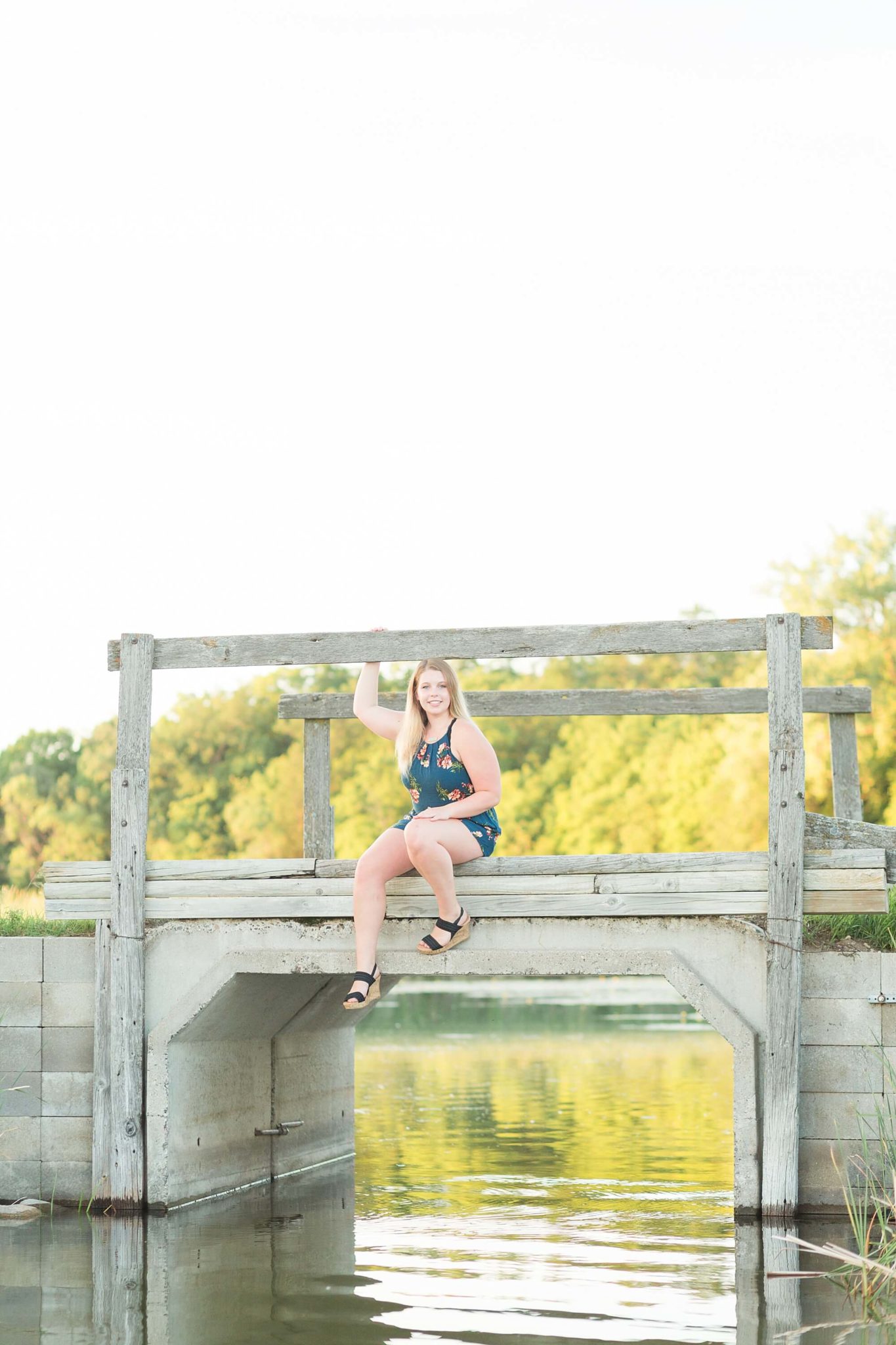 A High school senior sits on a wooden bridge over a lake for her senior portrait session