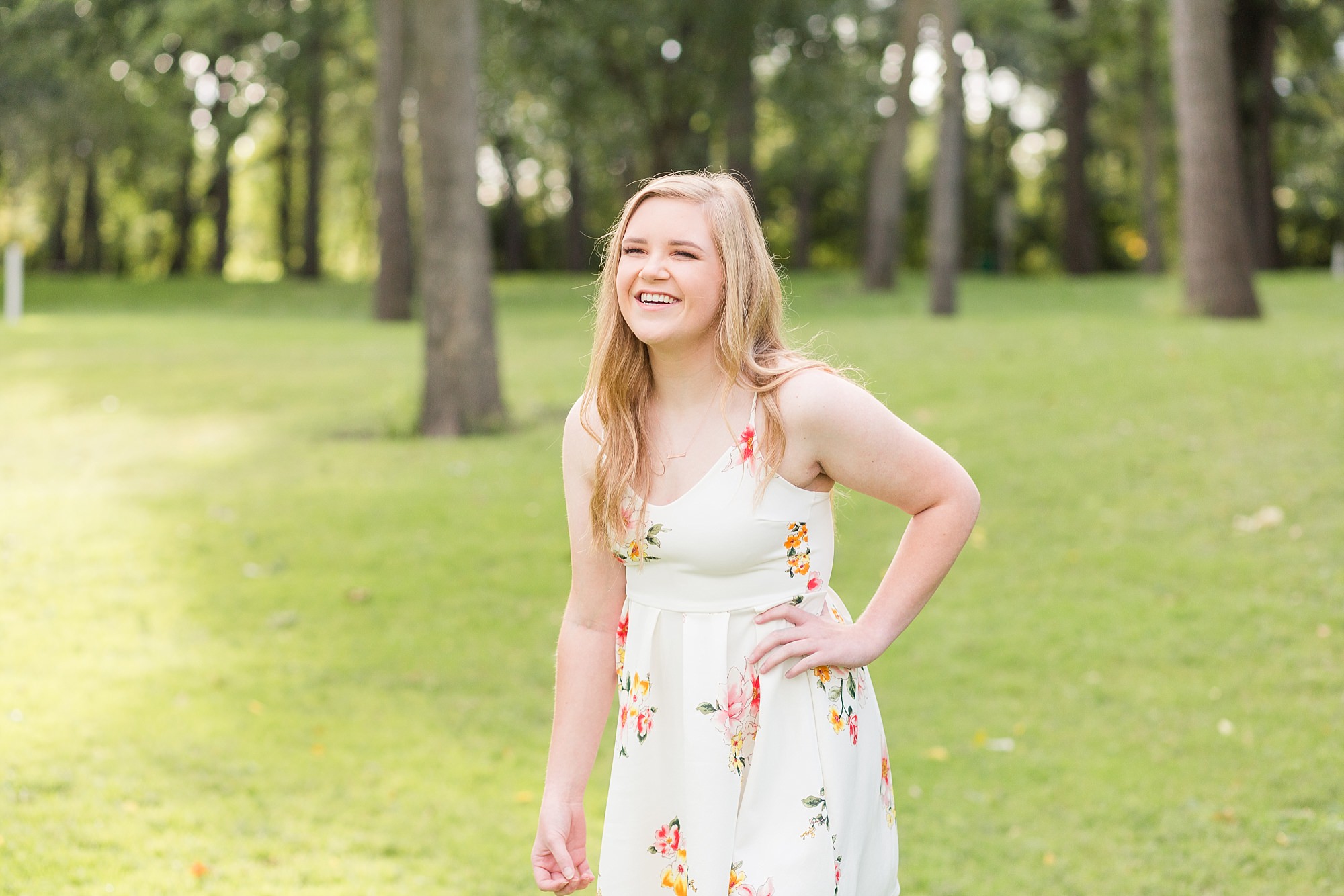 Senior girl laughs in white floral dress in Oak Grove Park, Fargo, ND