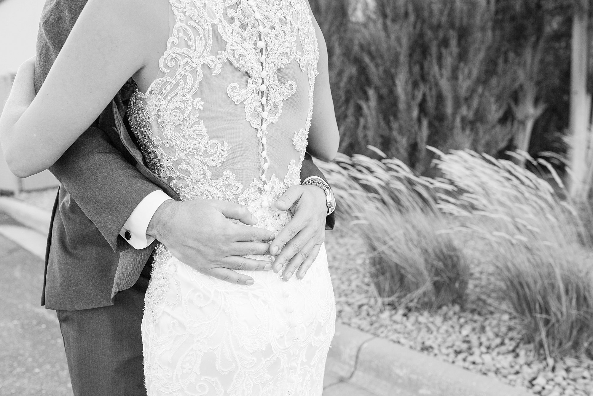 A groom's hands rest on his bride's back during their first look in black and white