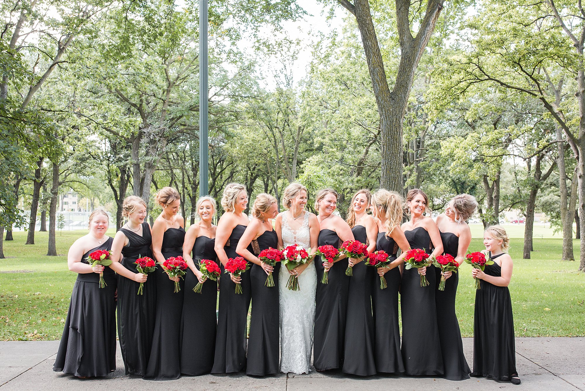 Bridesmaids in black glamorous dressed hold red rose bouquets
