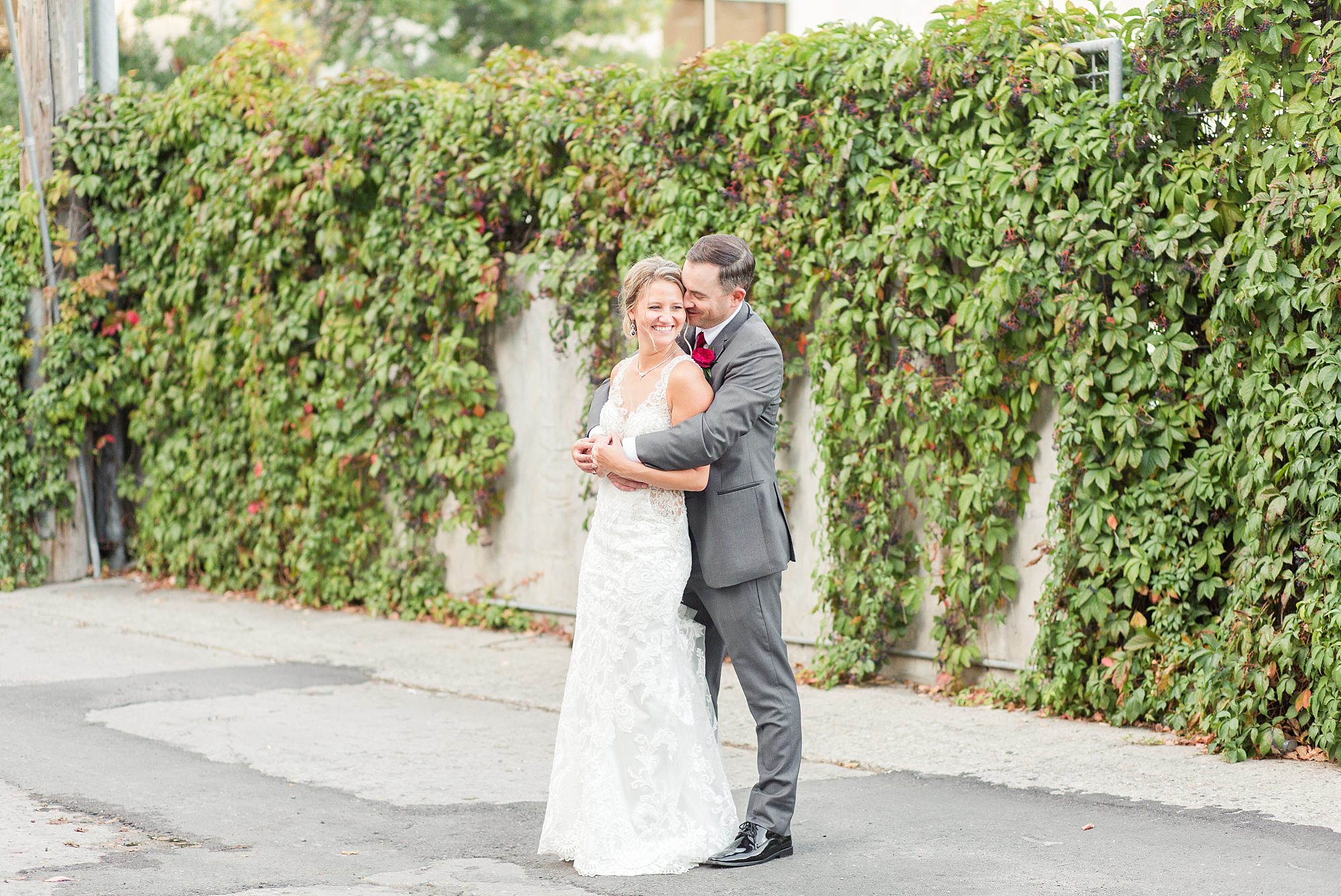 A groom holds his bride tightly near a vine covered wall in Downtown Fargo
