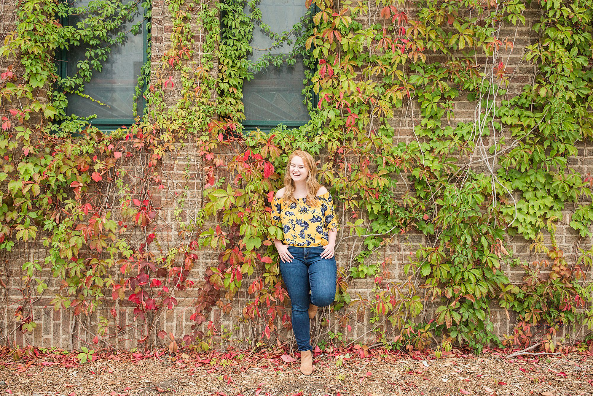 Senior in yellow and blue floral shirt leans against an ivy wall in Downtown Fargo