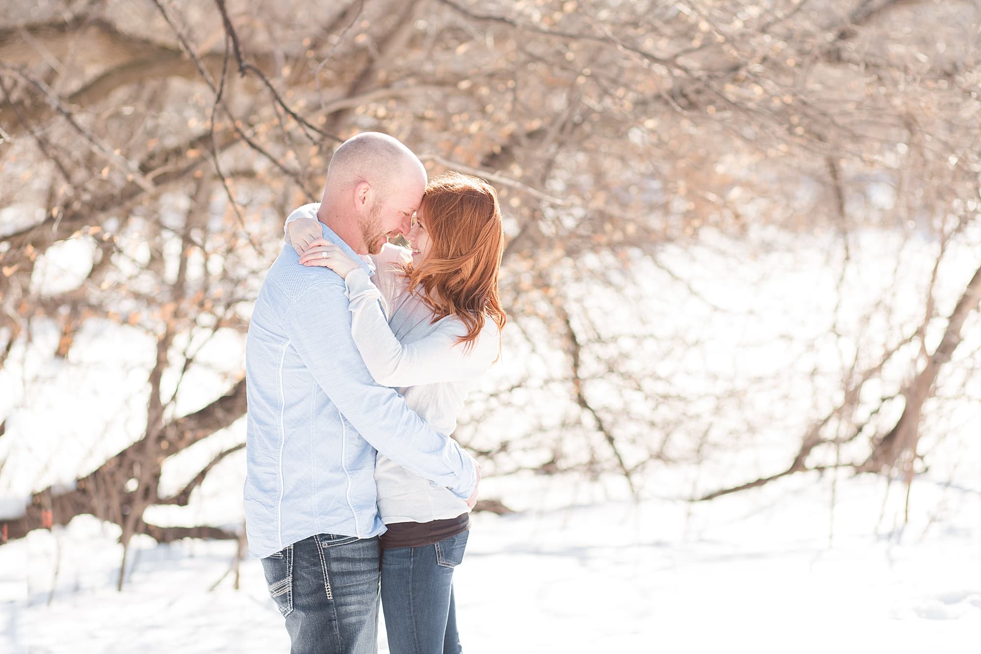 Engaged couple in pale blue and cream hold onto each other in a snowy park