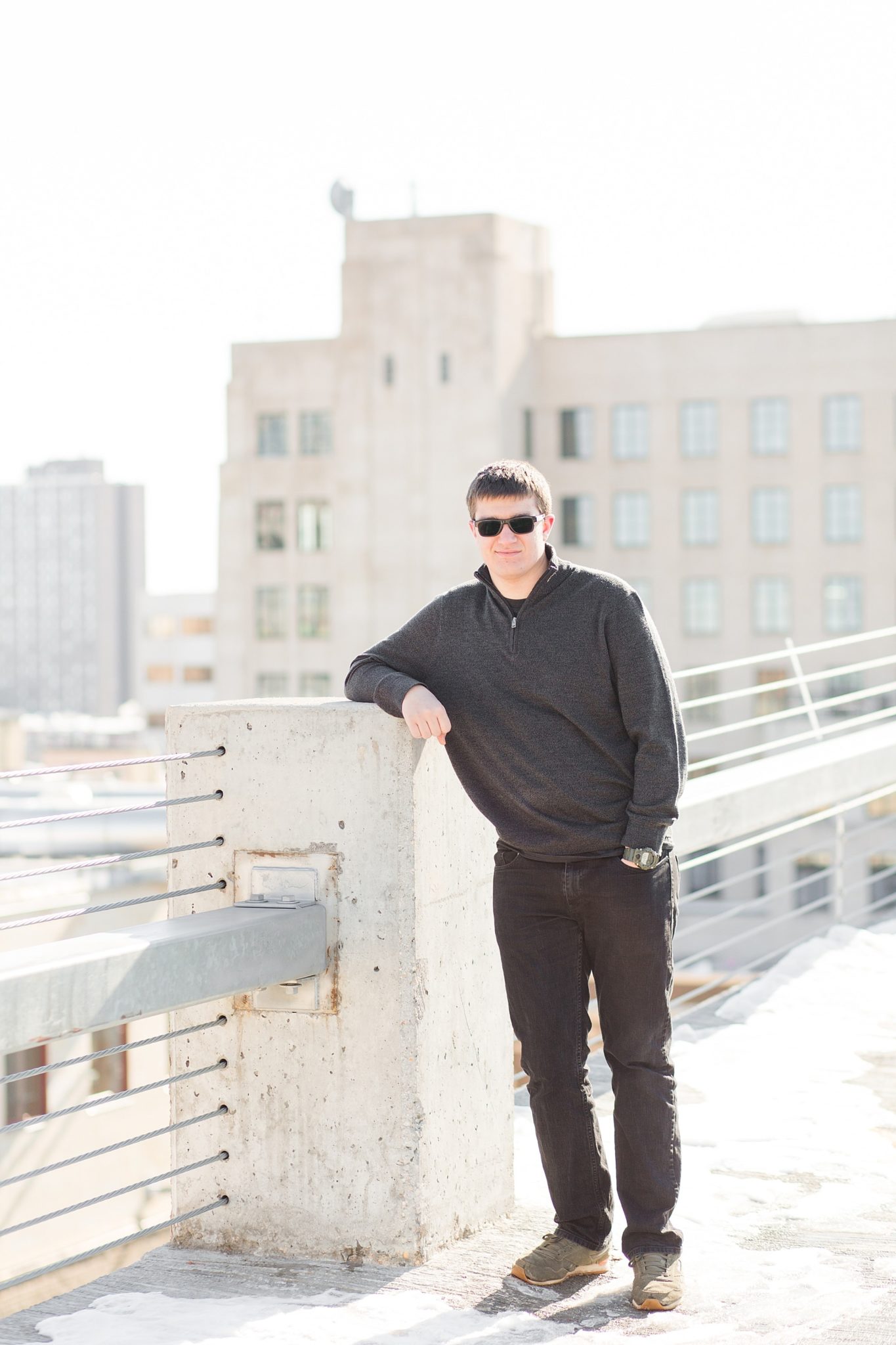 A senior guy leans on a concrete post in Downtown Fargo for his high school senior session