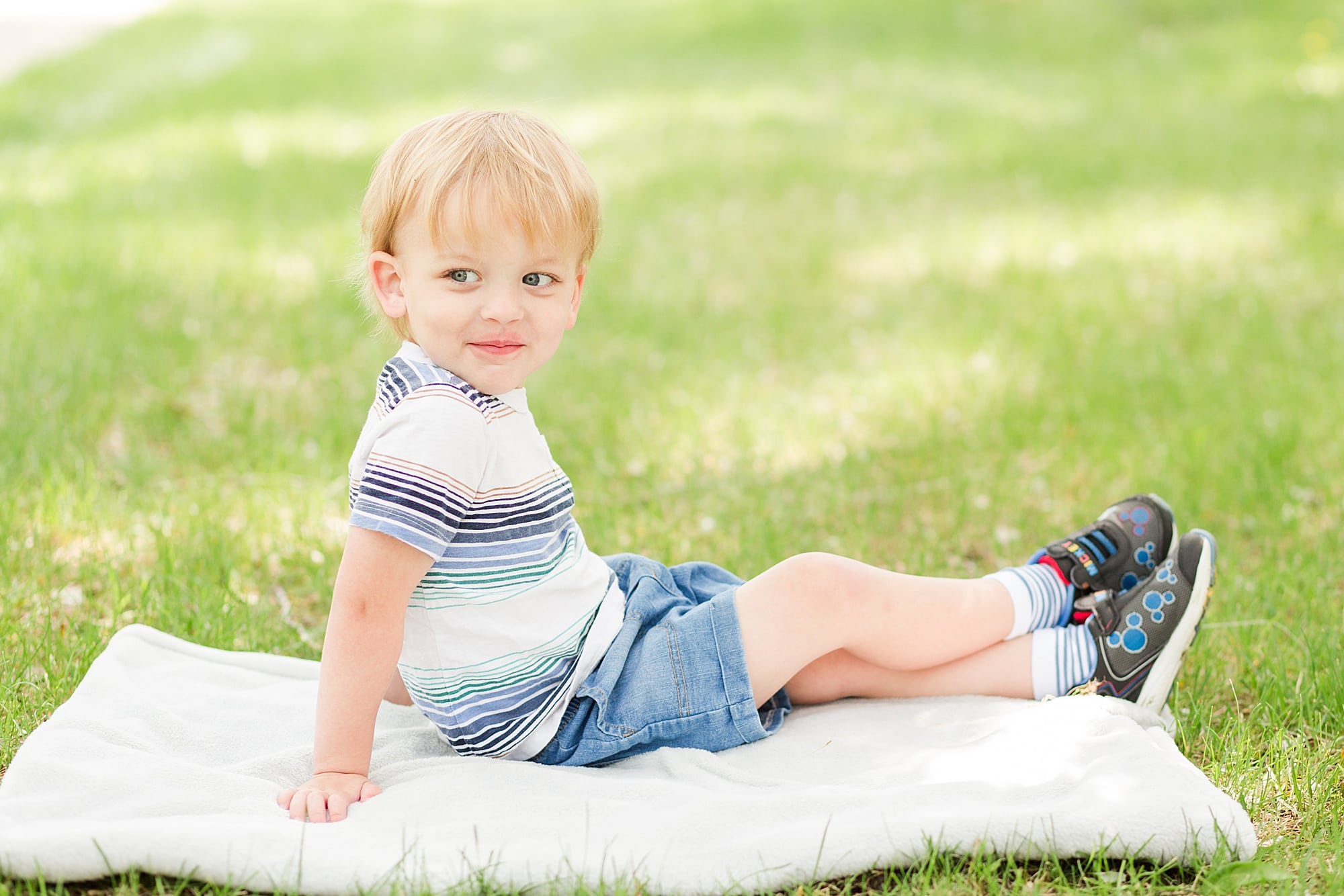 Three year old in striped shirt smiling in the grass