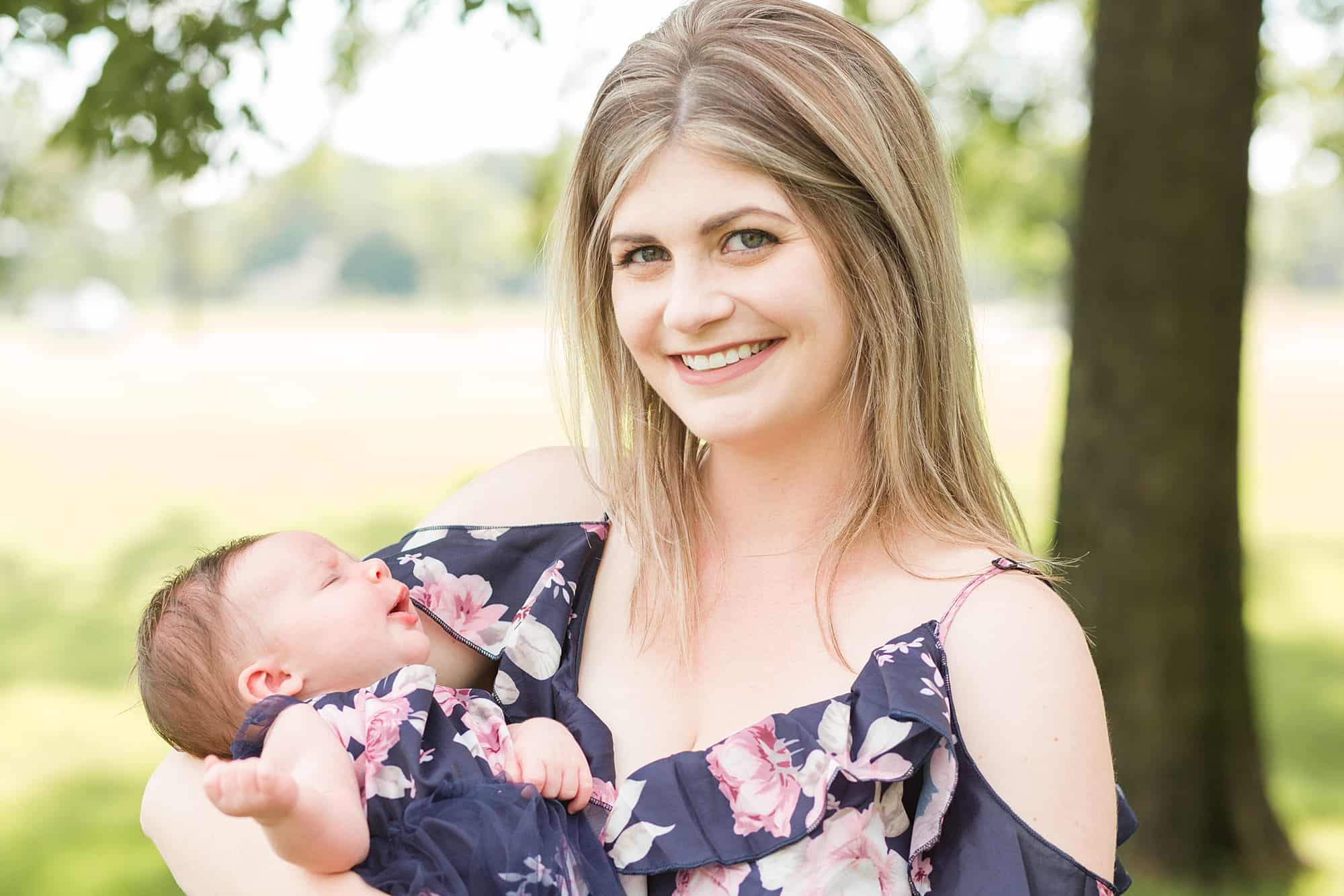 A new mom in a navy floral dress holds her newborn daughter in Lindenwood Park