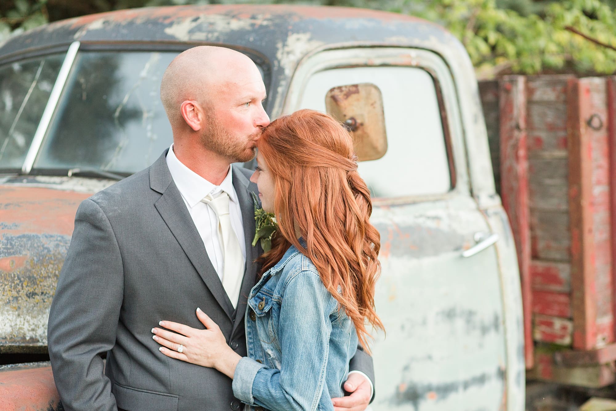 Bride wears a jean jacket over her dress as her groom kisses her on her forehead
