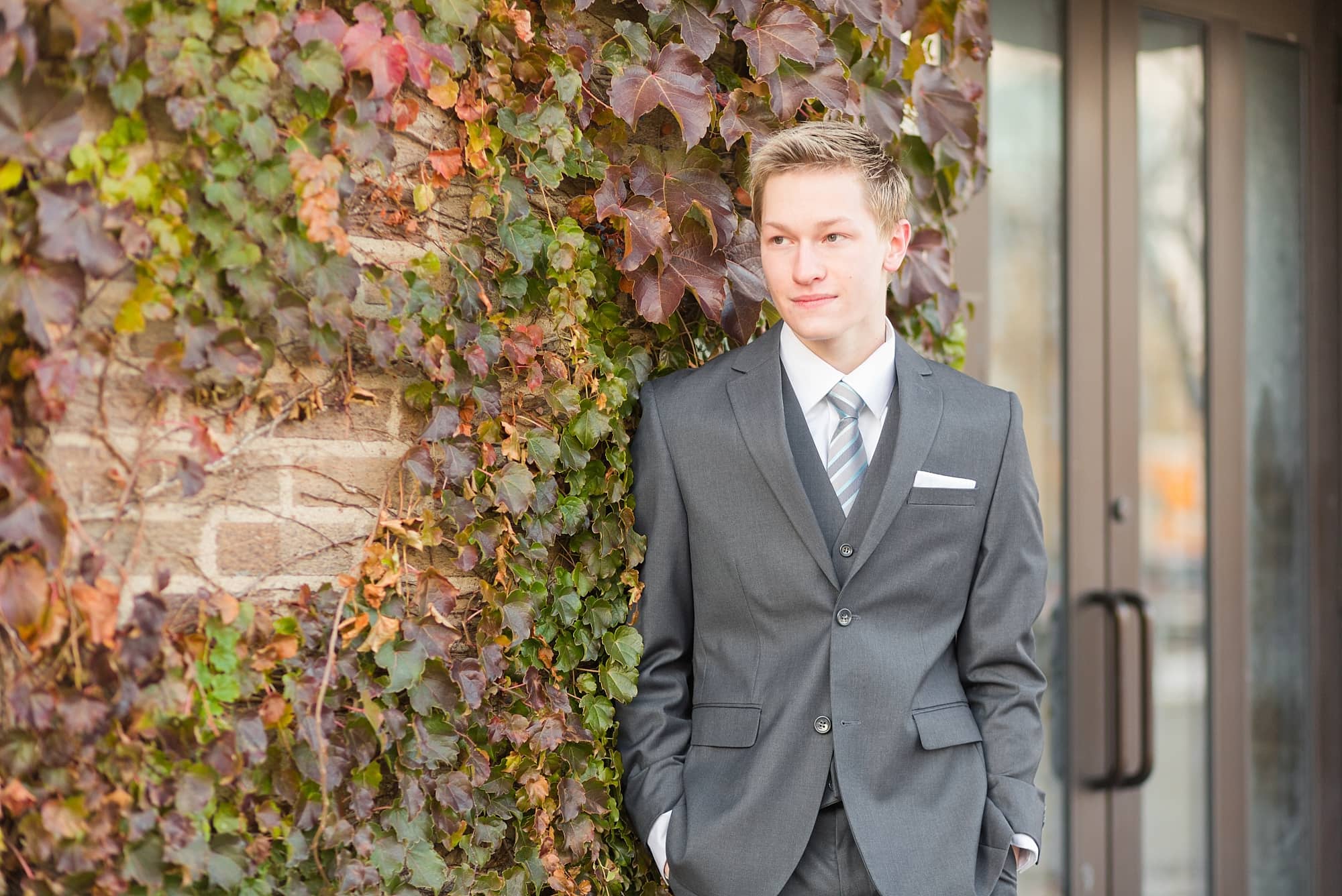 High School senior in grey suit and blue tie leans again colorful vines in Downtown Fargo