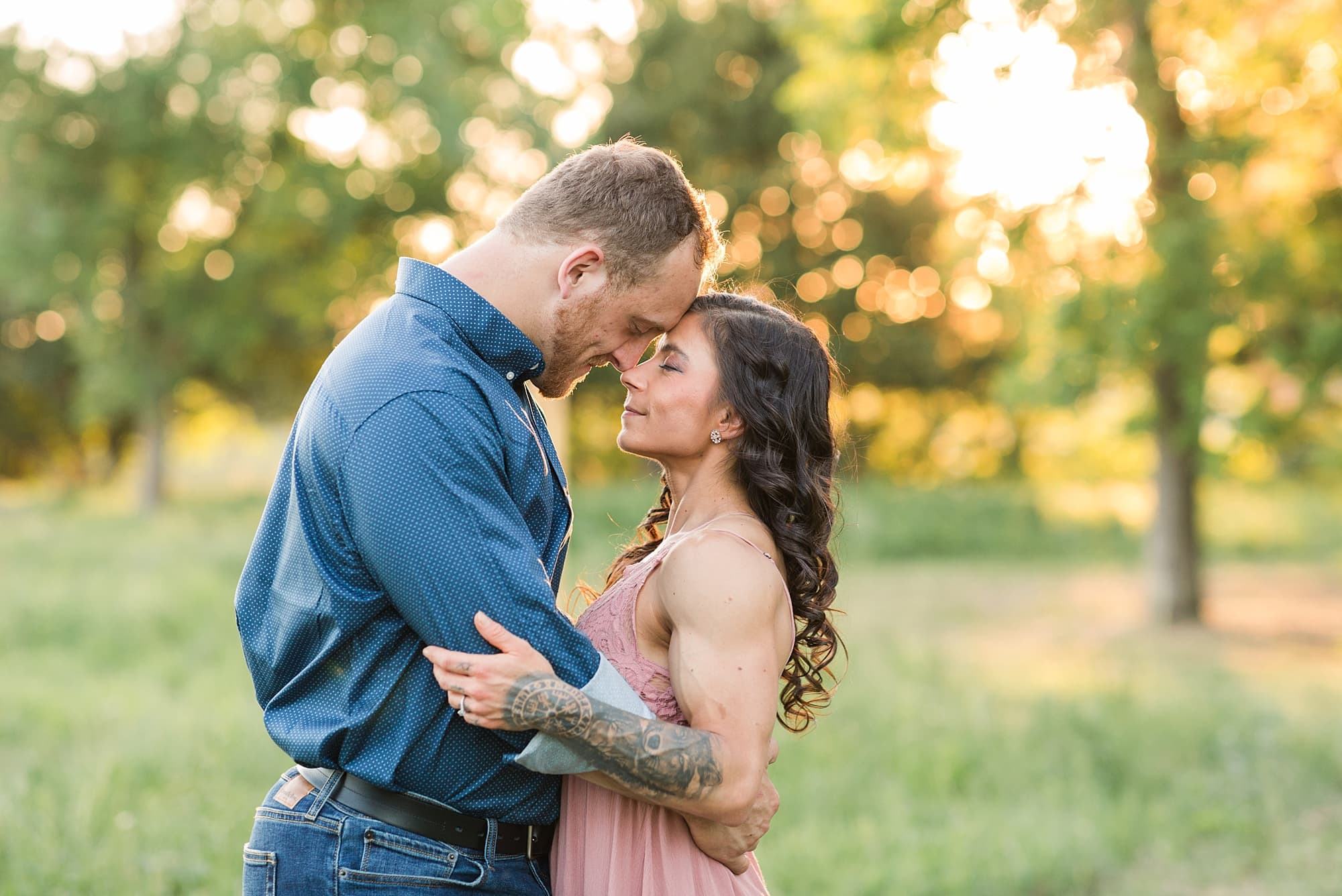 A couple lean into each other with the sunset coming through the trees in the background during their Engagement Session in Lions Conservancy Park