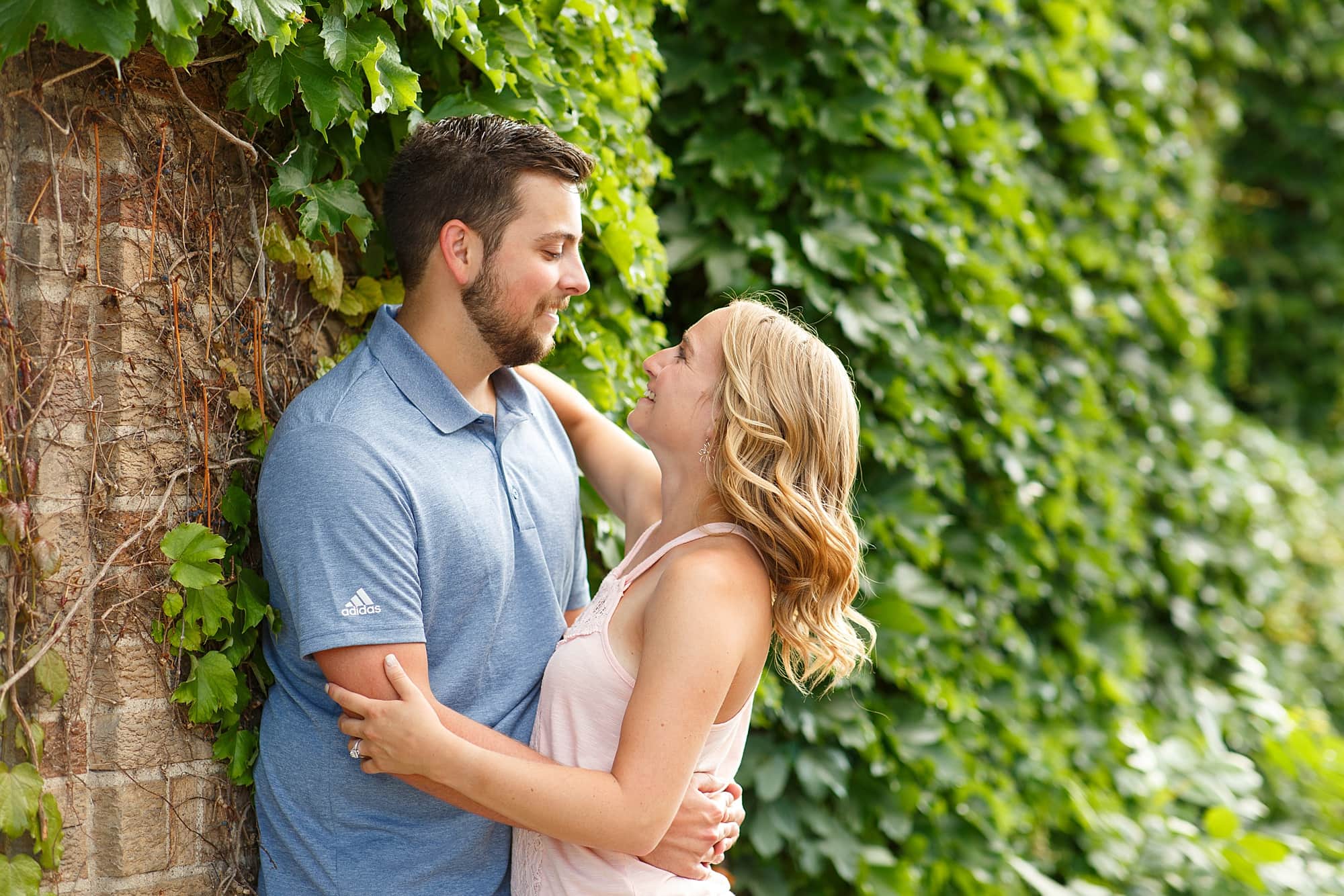Couple smiles at each other in front of an Ivy covered building during their Downtown Fargo engagement session