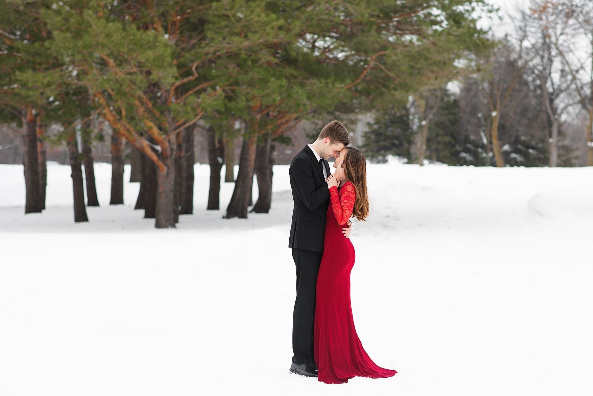 Engaged Couple in red dress and black suit in a snow filled park