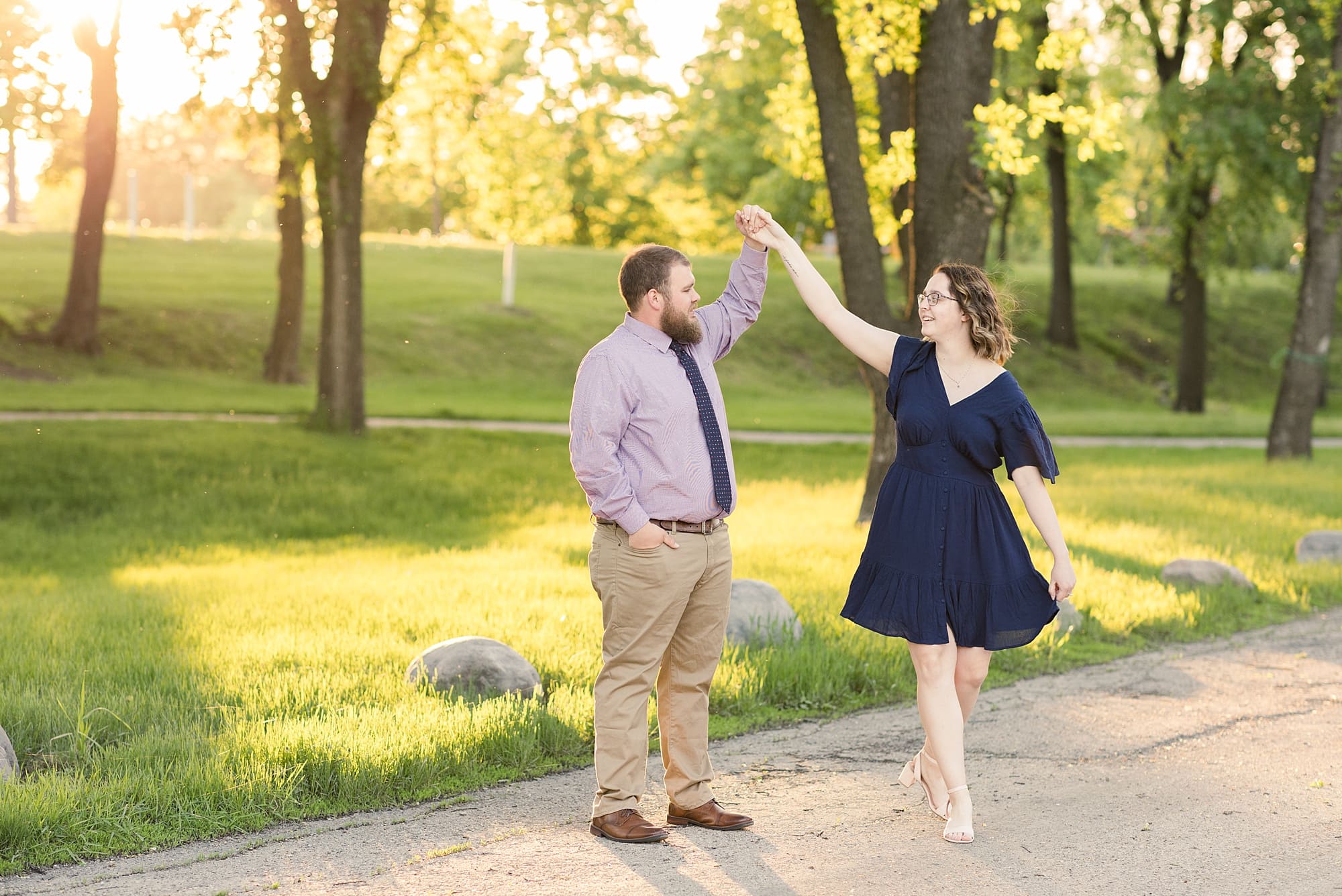 A couple in a navy dress and striped shirt dance during sunset at Lindenwood Park