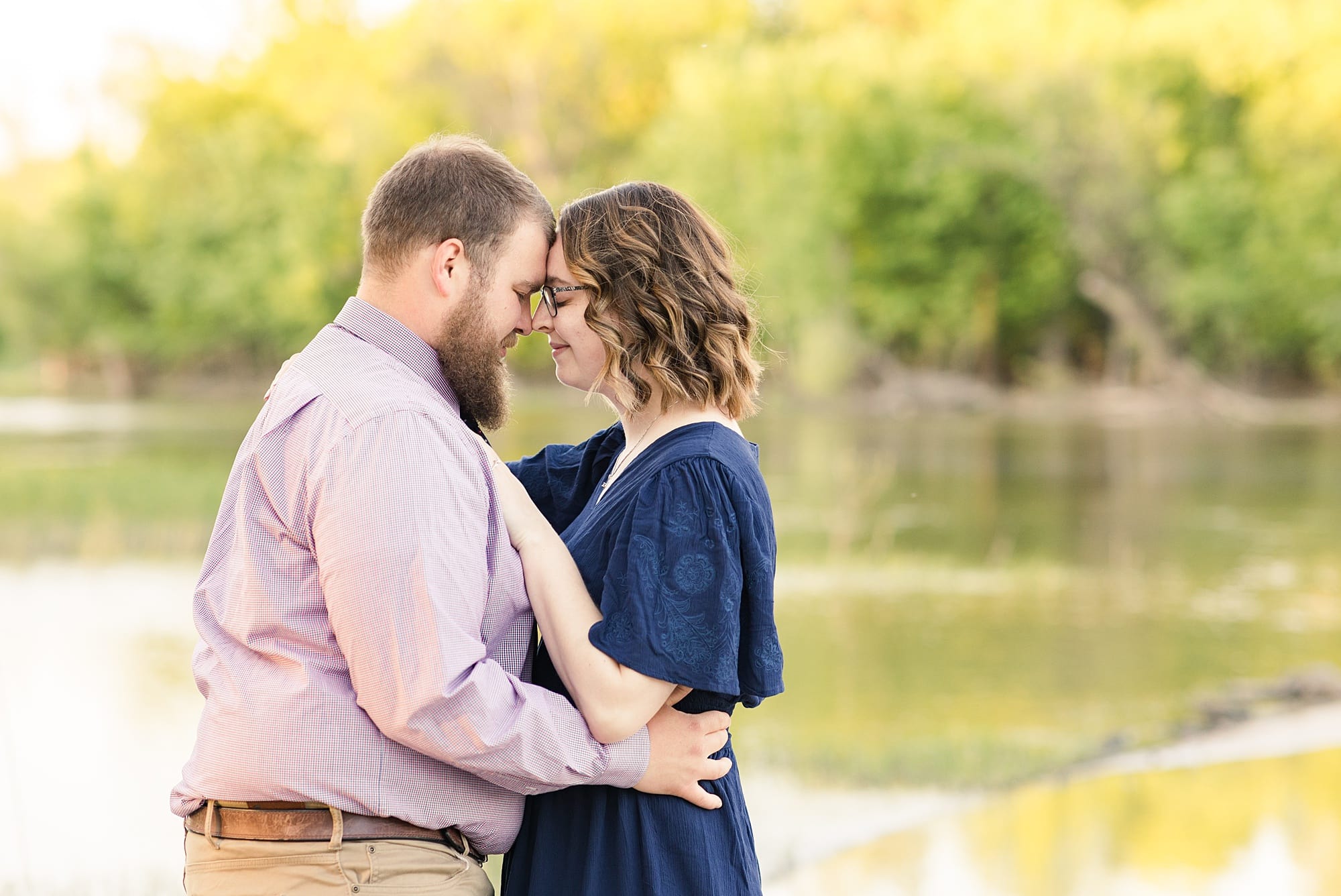 A couple embraces in front of the Red River at Lindenwood Park during their engagement photos