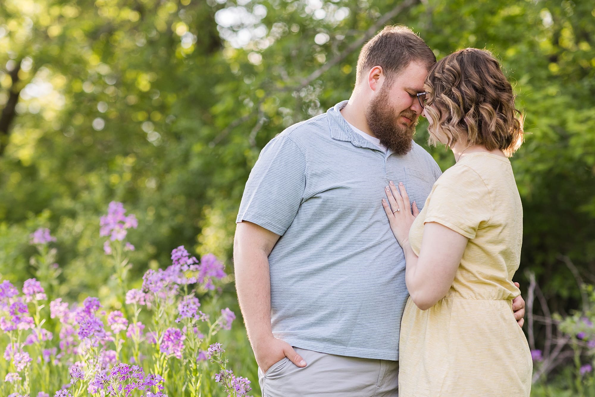A couple rests their foreheads together in a field of purple flowers during their engagement session at Orchard Glen
