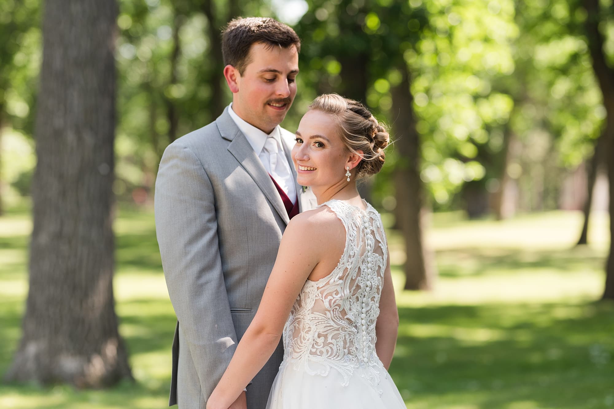 Bride in a halter lace wedding dress and her groom in light grey smile in Island Park

