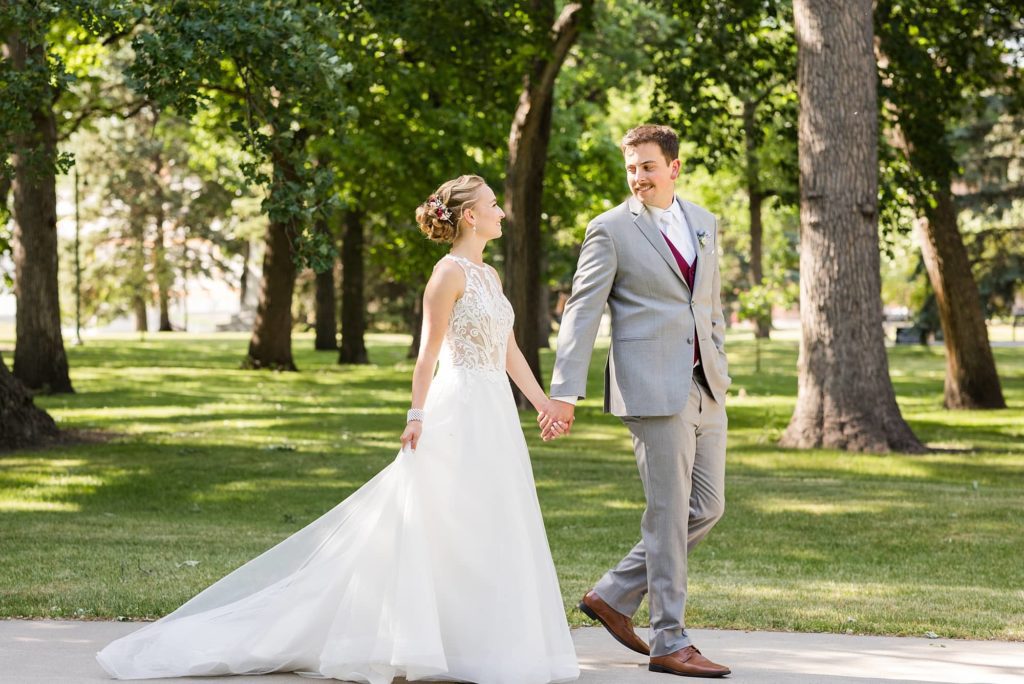 Bride and groom walk holding hands through Island Park, Fargo, ND