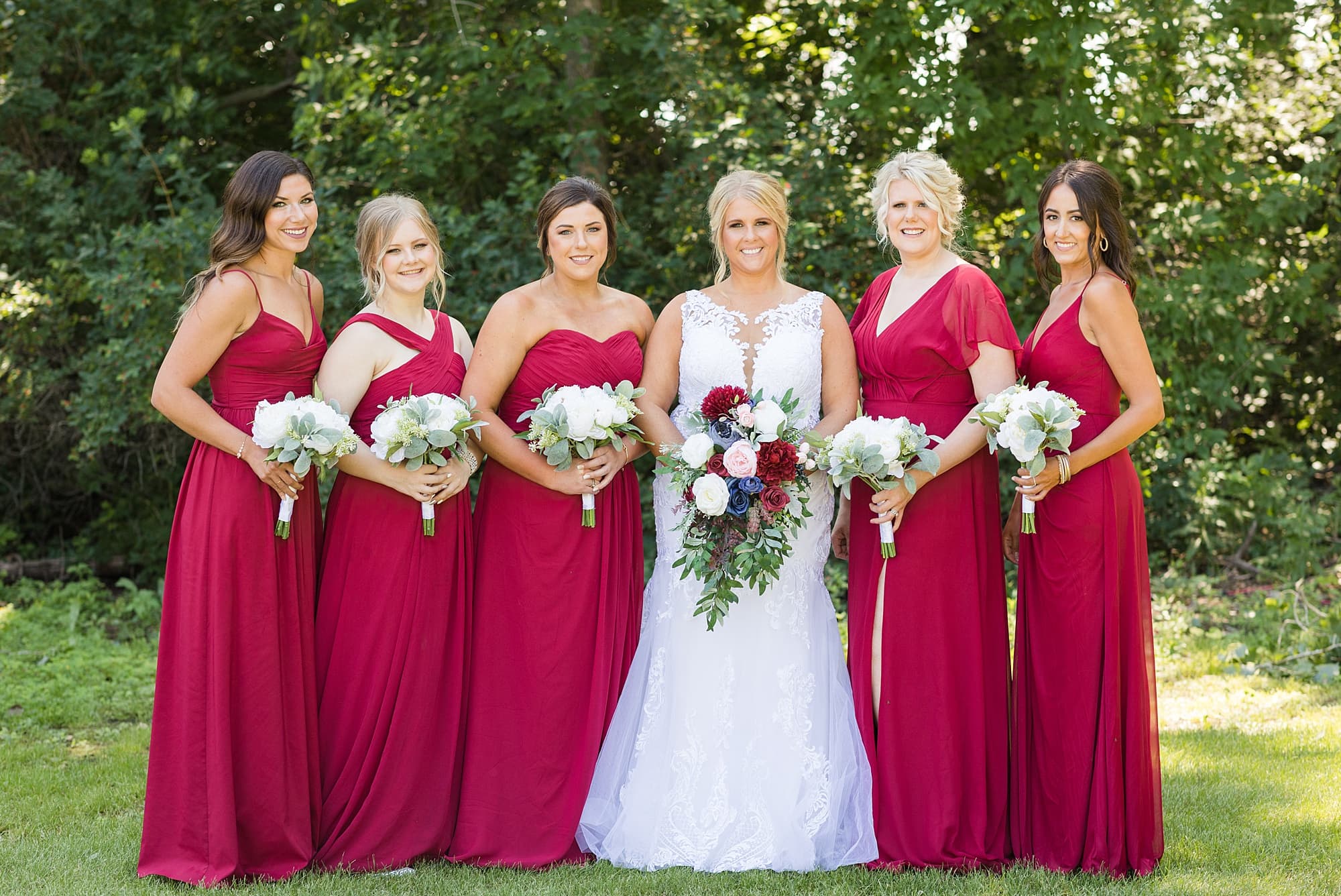 Bride and Bridesmaids in burgundy smile and hold their white flowers at Naastad Acres