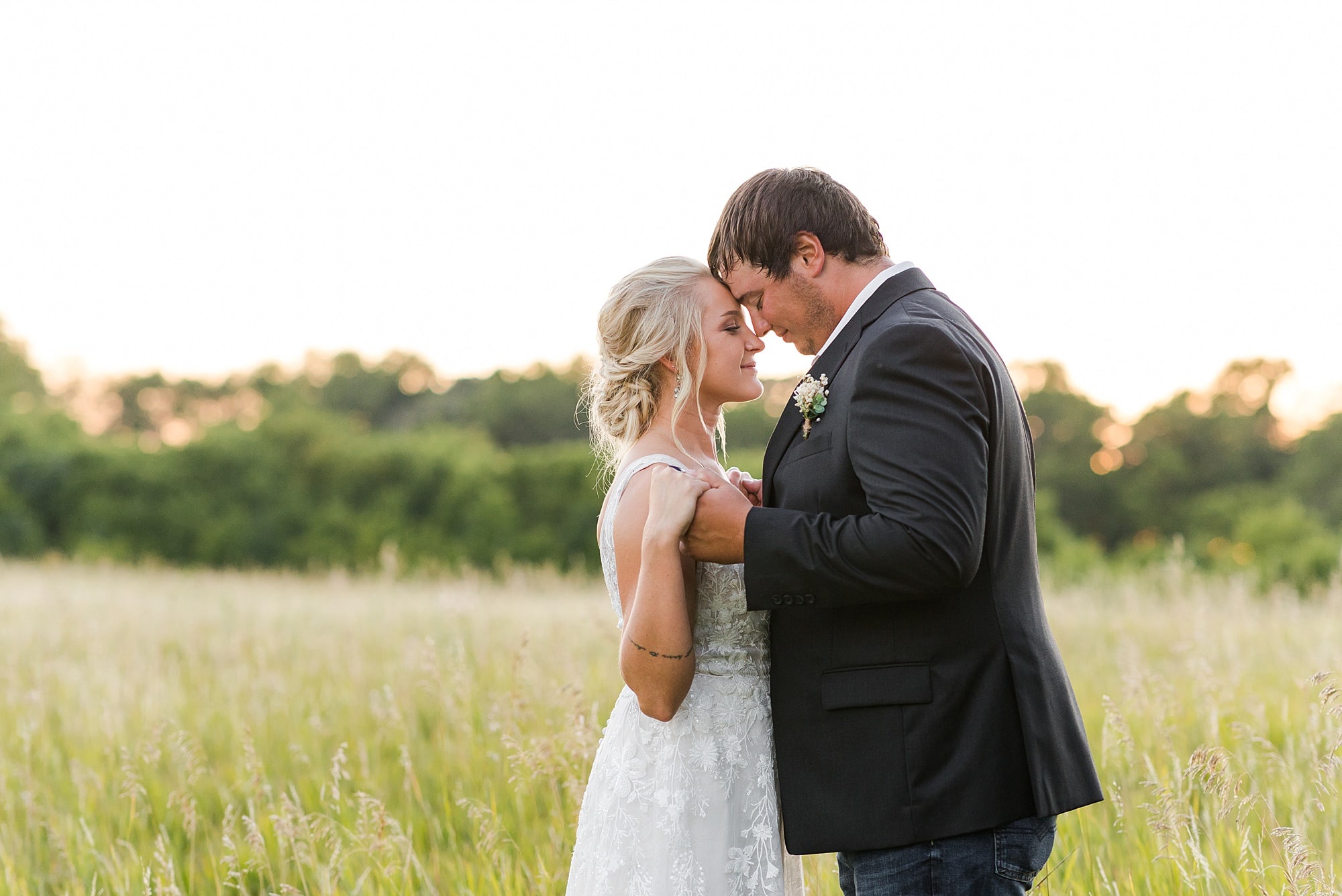 Bride and Groom hold hands and touch foreheads during sunset at Rustic Oaks