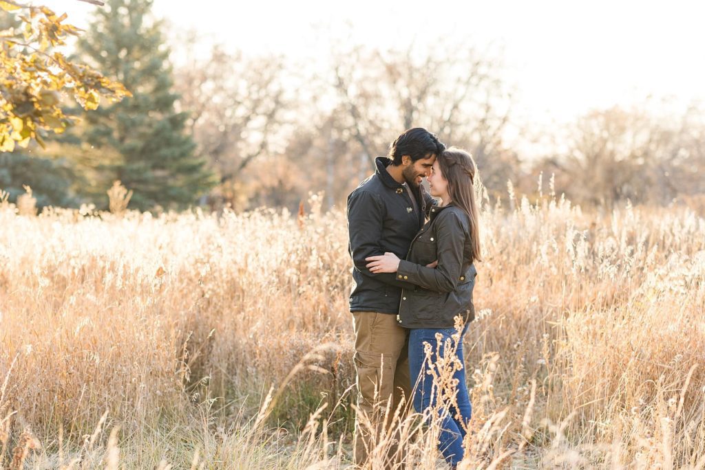 Engaged couple stand in tall gras and rest their foreheads together in Orchard Glen Park during their engagement session