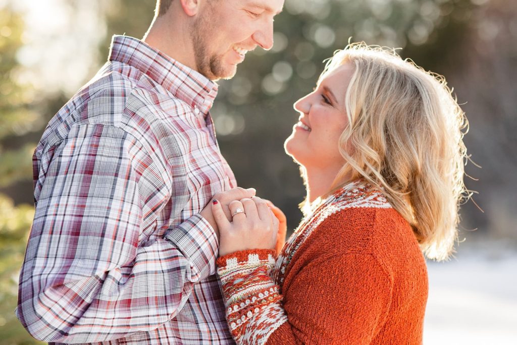 Couple holds hands and show off their engagement ring at their farm winter engagement session
