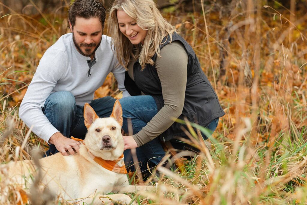 Engaged couple pet their dog during their Engagement Photos at Forest River Park