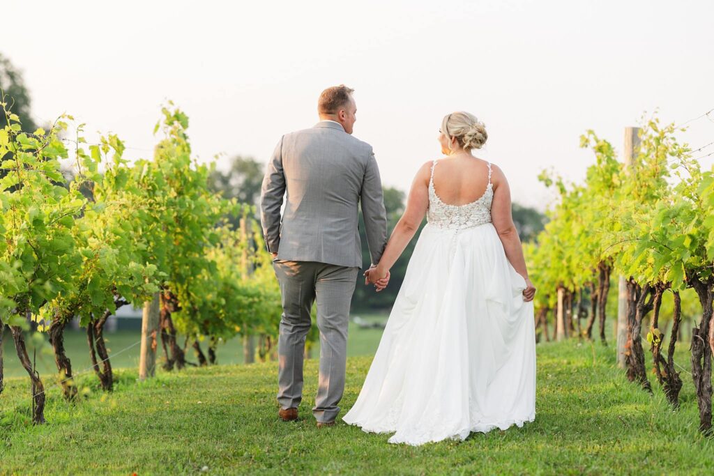 Newly married bride and groom walk through the orchard at their wedding at Carlos Creek Winery