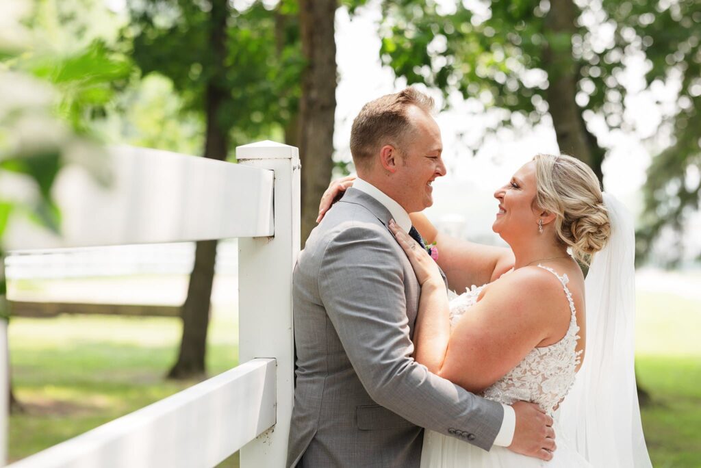 Bride and groom smile along a white fence a their wedding at Carlos Creek Winery
